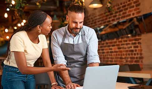 A restaurant manager speaks to an employee as they look at a laptop