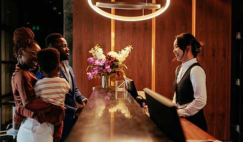 A front desk worker at a hotel smiles as she talks to a family who is checking in